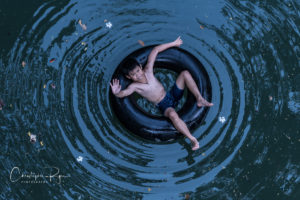 shirtless boy on inner tube in a river