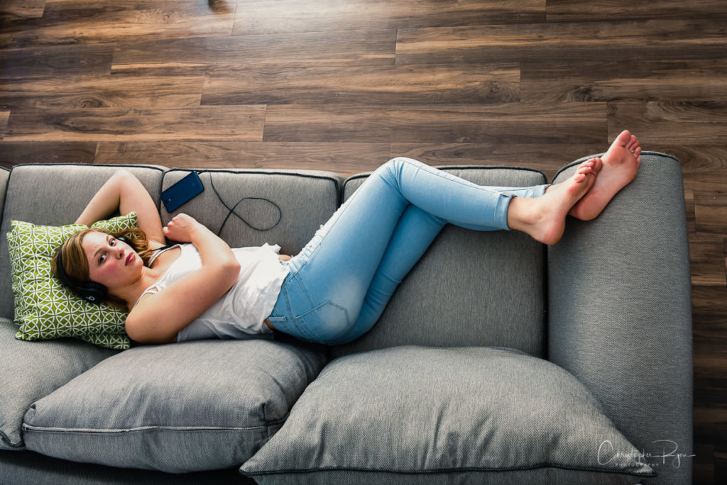 barefoot teen girl listening to music with ear buds on a grey sofa with no shoes