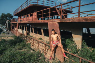 hull of rusty abandoned boat on the mekong river with cute shirtless teenage boy on the Mekong River.