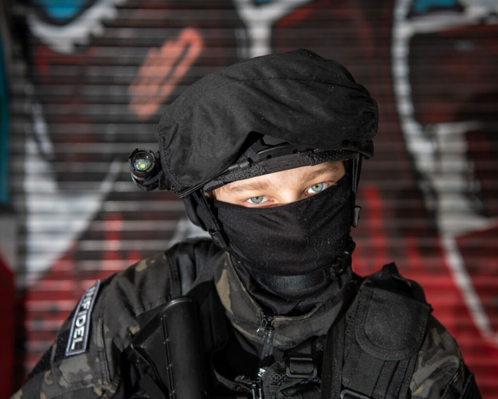 military man in balaclava in front of graffiti