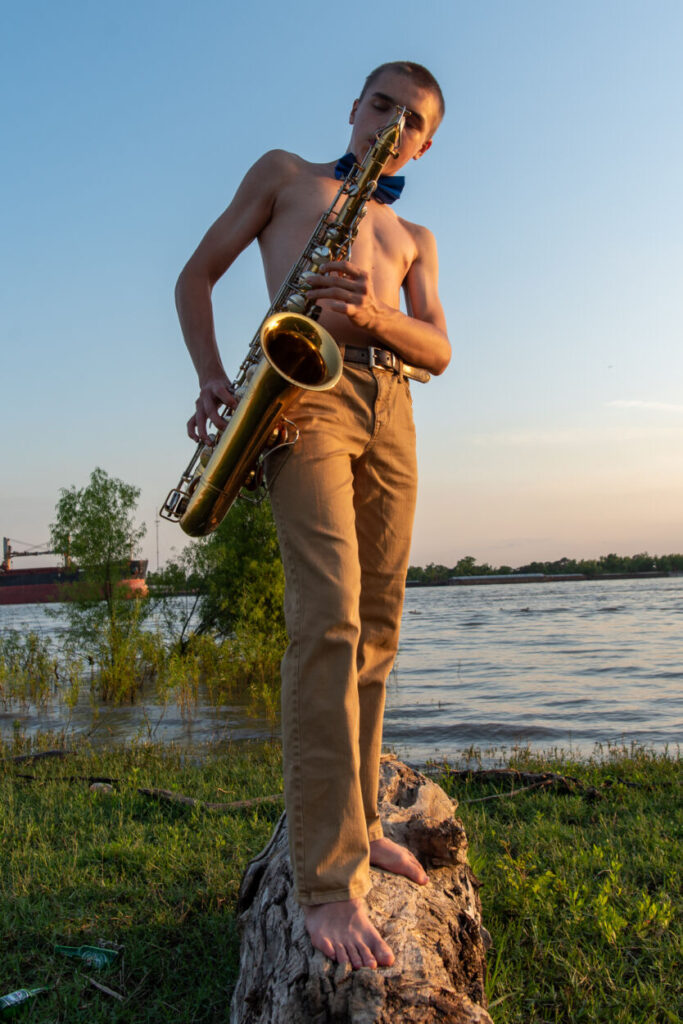 barefoot shirtless saxophone player with a bowtie in front of river