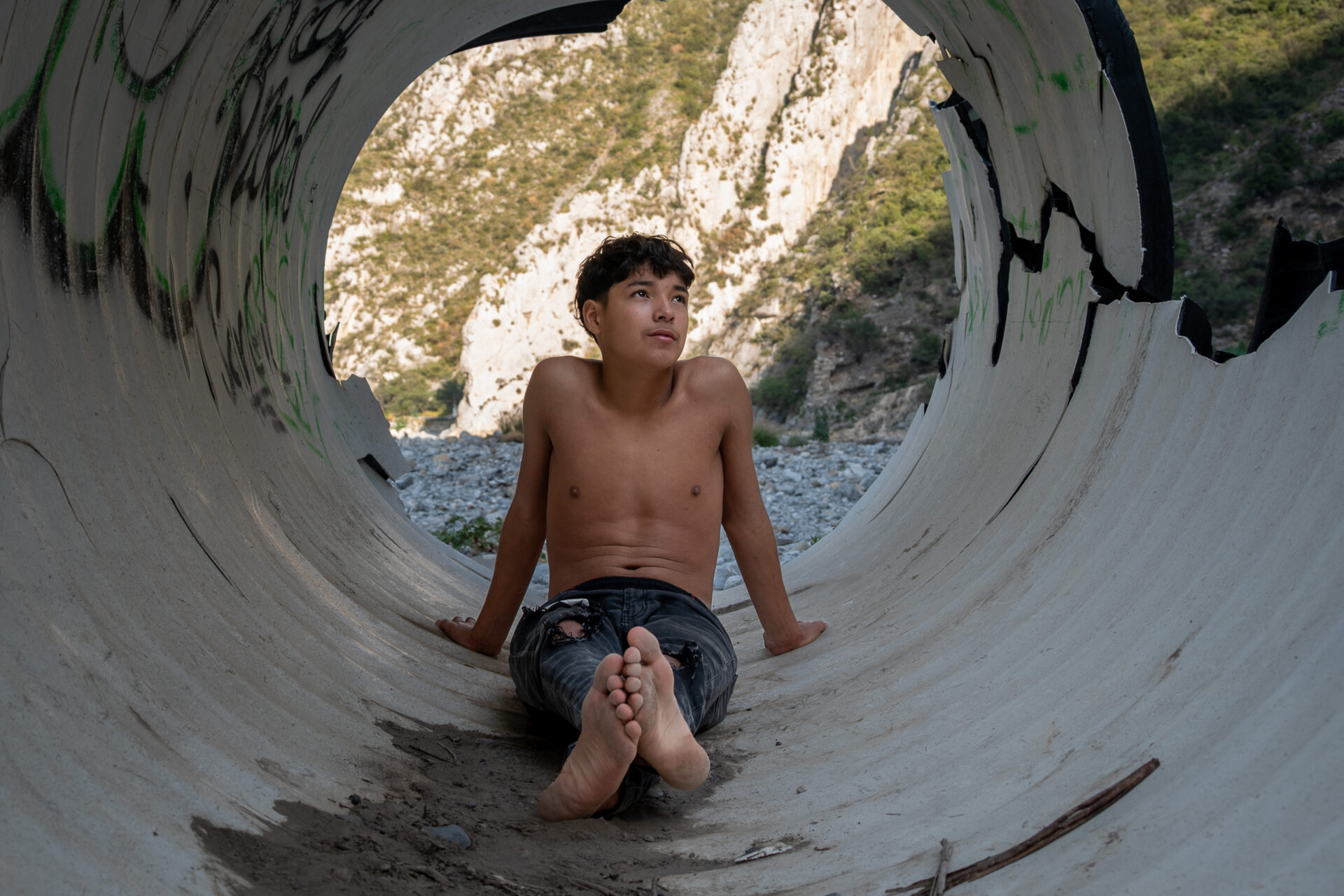 Boy sitting inside a large circular concrete culvert.