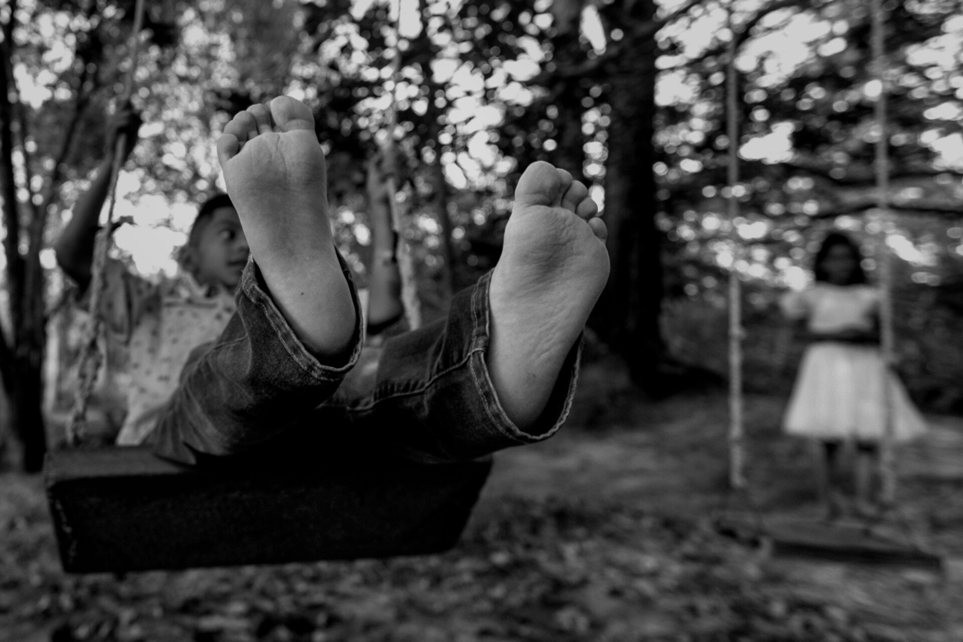 Black and white portrait of barefoot boy on a swing with his feet stretched out to the viewer.