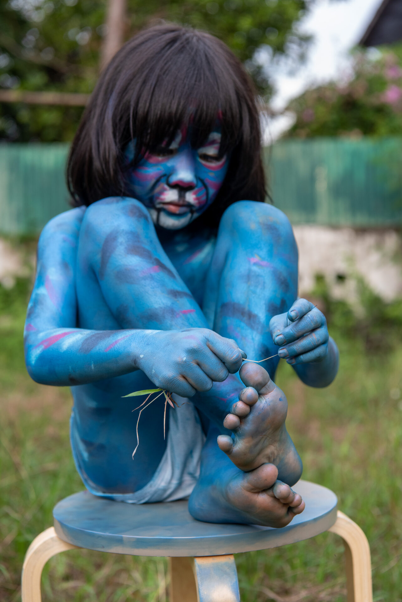 Child painted entirely in blue sitting on a wooden stool.