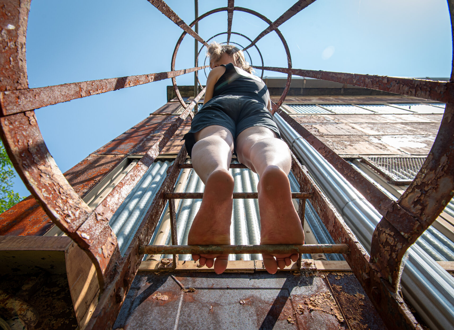 Young lady climbing a weathered, rusty industrial ladder.