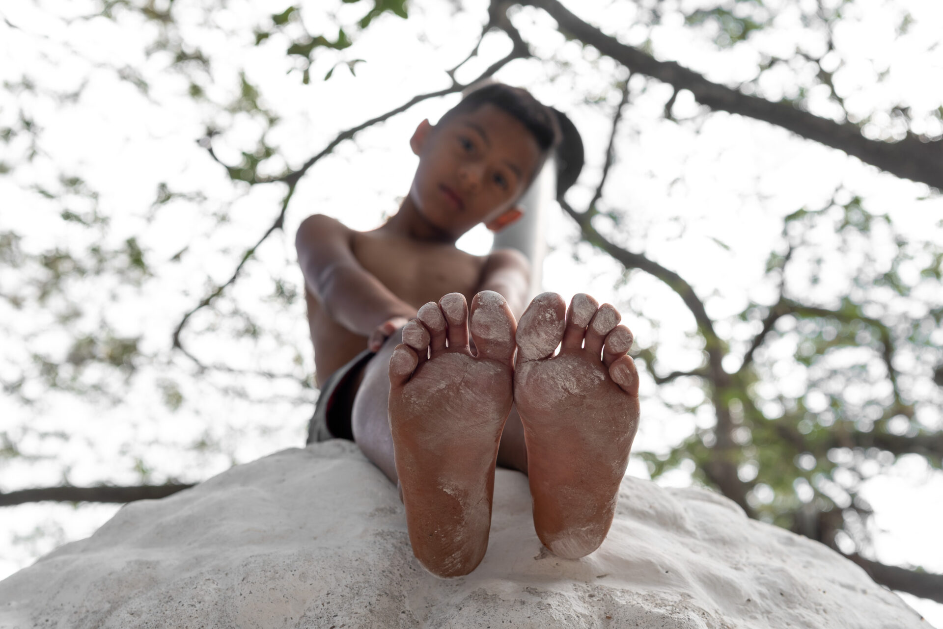 Young boy sitting on an outdoor oven with the soles of his feet towards the viewer.