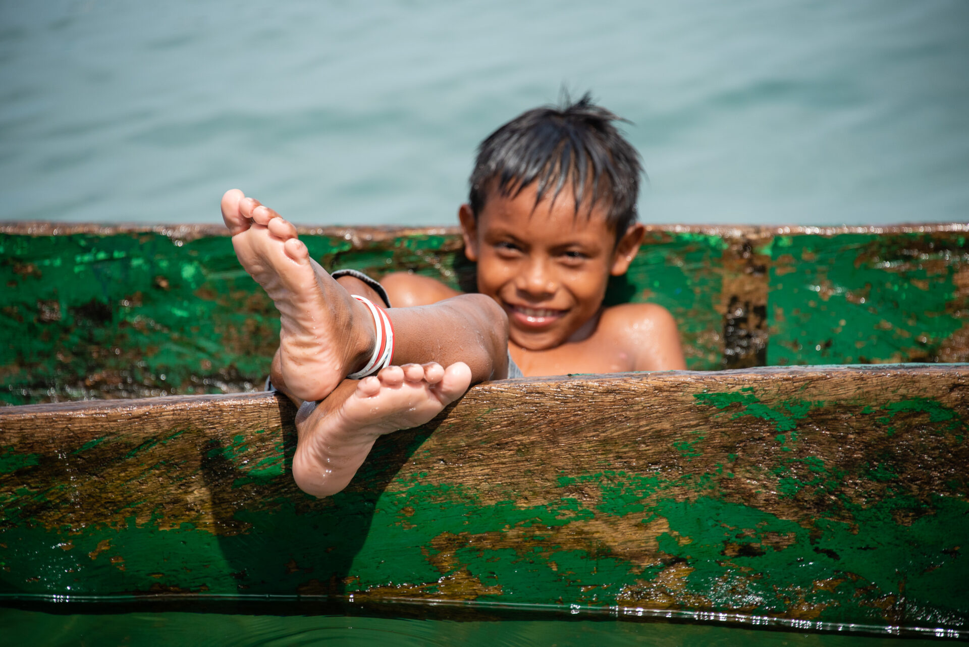 Kuna Indian boy with wet feet sitting in a weathered green wooden boat.