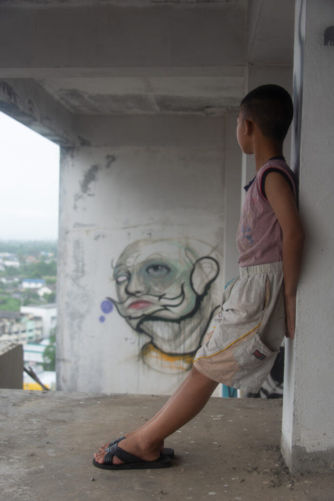 Profile portrait of a young boy leaning against a concrete pillar at the abandoned Ghost Tower in Chiang Mai.